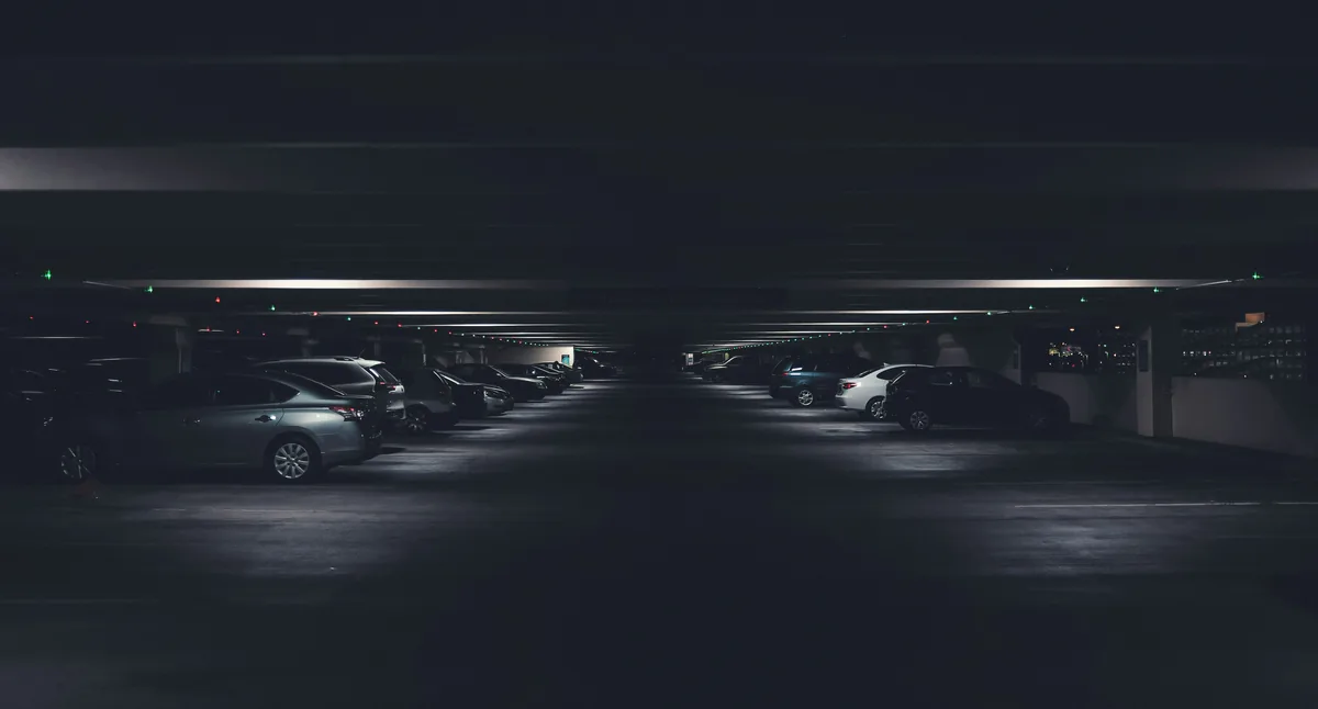 A wide underground garage lined with cars at night